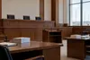 An empty appellate courtroom with unmarked legal briefs on counsel tables and power lines visible through a window.