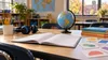 An open blank workbook, pencils, headphones and a globe on a classroom table in an Indiana school.