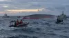 Indonesian search-and-rescue vessels surround an overturned passenger ferry in rough Java Sea waters at dawn.
