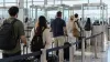 Travelers queue at an unbranded airport border inspection area in natural daylight