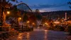 Illustrative autumn amusement park at dusk with a wooden roller coaster, pumpkins and light theatrical fog.