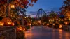 Illustrative twilight theme park walkway lined with glowing pumpkins and a roller coaster in the distance