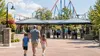 An adult and two children walk toward the entrance of a regional amusement park with a roller coaster in the background.