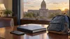 An unbranded smartphone, closed budget binder and child’s backpack on a desk with a state capitol building visible through the window