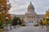Kentucky State Capitol in Frankfort framed by autumn trees under an overcast sky