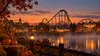 Illustrative autumn amusement park at dusk with a roller coaster silhouette, pumpkins and warm midway lights