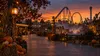 Autumn amusement park midway with pumpkins, warm lights and a roller coaster silhouette at blue hour