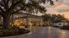 A generic institutional building with a covered entrance and unbranded service vans beneath live oak trees at dusk