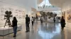 Visitors explore a contemporary narrative-art gallery with a vintage film camera, storyboard panels and an original spacecraft-like sculpture.