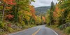 A quiet rural road through a mixed Maine forest showing green, yellow, orange and red late-September foliage.