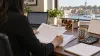 Payroll manager reviewing records at a desk overlooking a Maryland harbor
