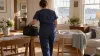 A visiting nurse approaches a newborn bassinet in a sunlit Massachusetts home.