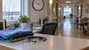 A quiet nursing-home staff work area with folded scrubs and a stethoscope beside a softly lit corridor.