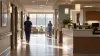Illustrative view of caregivers walking through a bright nursing home corridor beside a nurses' station