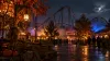 Generic amusement park midway and roller coaster illuminated at night with autumn trees and theatrical fog