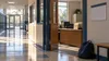 A quiet public school corridor beside an open attendance office, with blank files and a student backpack in morning light.