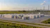 A generic utility-scale battery storage installation beside an electrical substation and farmland.