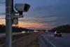 Unbranded roadside traffic camera beside a divided highway at dusk