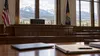An empty courtroom bench with a closed laptop and documents, with a Montana landscape visible through windows.