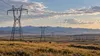 Transmission lines crossing a Montana landscape beneath a neutral evening sky