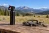 An unbranded bear-spray canister and an unset wildlife trap on a field table beside a Montana mountain meadow.