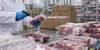 Gloved food-safety worker examining sealed raw meat packages in a refrigerated distribution warehouse