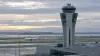 Unbranded airport control tower beside runways and a taxiing passenger aircraft at dawn.