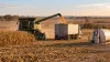 Corn harvest equipment loads grain into a truck beside a diesel tank on rural Nebraska farmland.