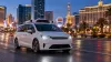 An unbranded autonomous electric minivan travels through Las Vegas at dusk with hotel towers in the background.