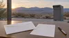 A blank mail ballot, envelope and pen on a table overlooking Nevada desert mountains with an unmarked drop box nearby.