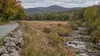 Low water in a rocky stream beside a dry field and early autumn forest in rural New Hampshire