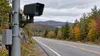 A roadside automated license plate camera overlooks a quiet New Hampshire road surrounded by autumn foliage.