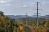 Steel transmission monopoles cross a wooded New Hampshire landscape in early autumn.