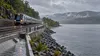 Illustrative commuter train traveling beside the Hudson River near reinforced shoreline and drainage infrastructure.