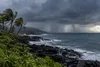 Dark tropical storm clouds and offshore rain bands approach a generic volcanic coastline in Hawaiʻi.