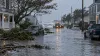 A flooded coastal neighborhood street after a nor’easter, with submerged vehicles and emergency crews working in gray morning light.
