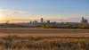 Harvested North Dakota prairie overlooking a small city, grain elevator, construction crane and oil pumpjack at sunrise