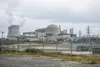 Generic distant view of a secured industrial nuclear research complex under an overcast sky, with utility buildings and infrastructure but no identifiable signs or people.