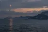 A distant generic missile rises above a rugged coastline at dawn in a restrained editorial scene.
