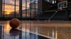 An empty college basketball court at sunset with a courthouse-like civic building visible beyond the arena windows.
