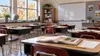 Empty public-school classroom with open reading books and math worksheets on desks in autumn light