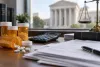 Unlabeled prescription bottles, a calculator and blurred invoices on a legal office desk with courthouse columns in the background.