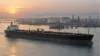 An unbranded crude-oil tanker passes a coastal energy terminal in early-morning light.