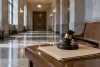 An empty courthouse corridor with closed courtroom doors, a plain case file and a wooden gavel on a foreground bench.