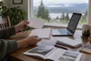 Hands sorting blank election-related envelopes beside a laptop in an Oregon home.