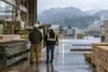 Illustrative view of two workers at an unbranded wood-products facility in Oregon’s rainy industrial landscape