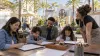 A family sketches together at an outdoor animation workshop in a generic palm-lined theme park courtyard.