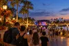 Visitors walk toward an outdoor concert stage along a palm-lined Florida theme-park promenade at blue hour.