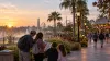 Visitors consult a phone and park map on a palm-lined Central Florida resort promenade at sunrise.