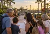 A multigenerational family reviews a blank itinerary and phone on a generic palm-lined Central Florida theme park promenade
